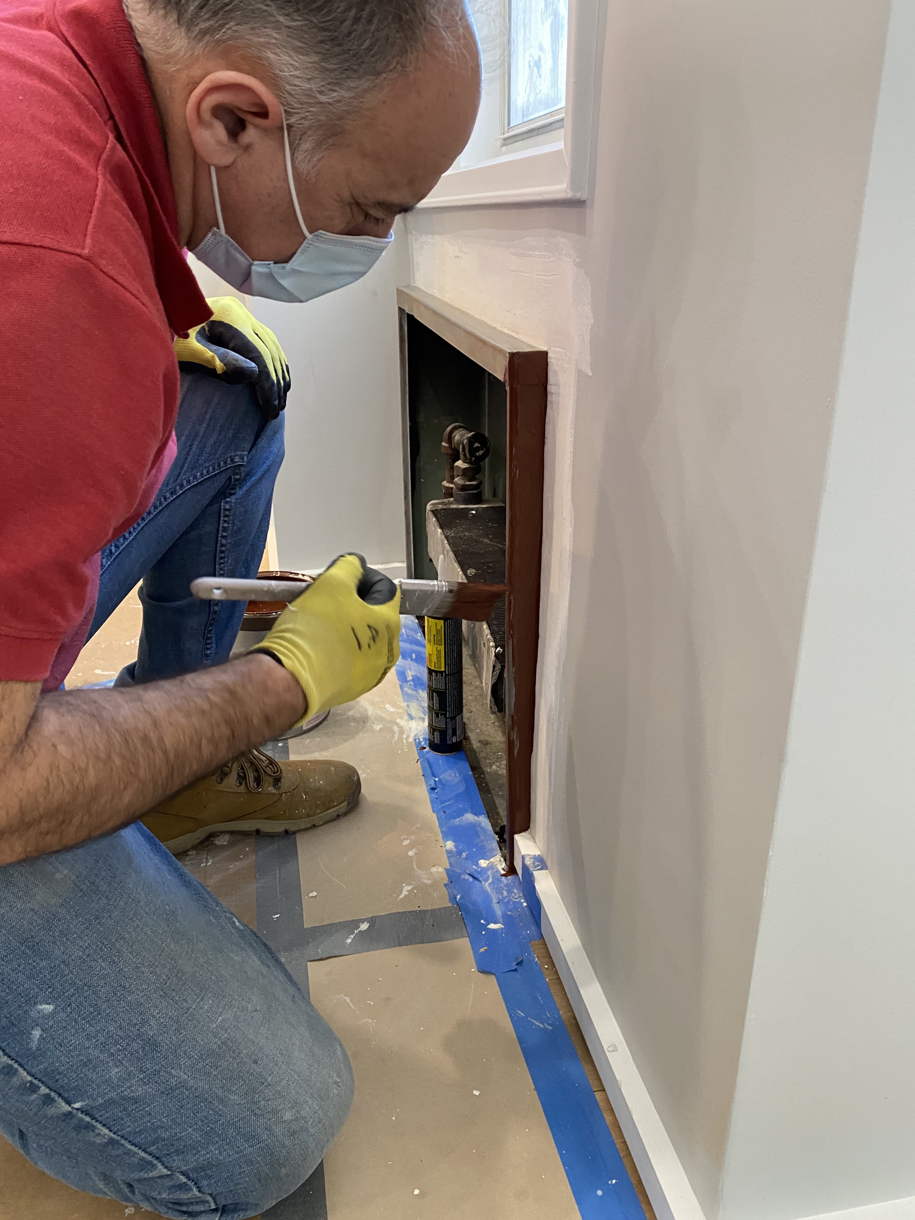 Worker painting radiator enclosure with protective floor covering